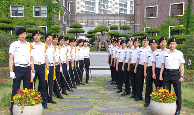 ROTC 학생들이 건물앞에서 십일자형태로 서로 나란히 줄지어 서 있다.